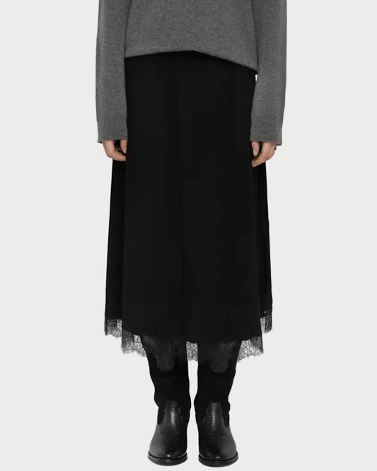 A model stands against a light gray studio background wearing a gray knit sweater, a long black skirt with a sheer tulle hem, black leggings, and black ankle boots.