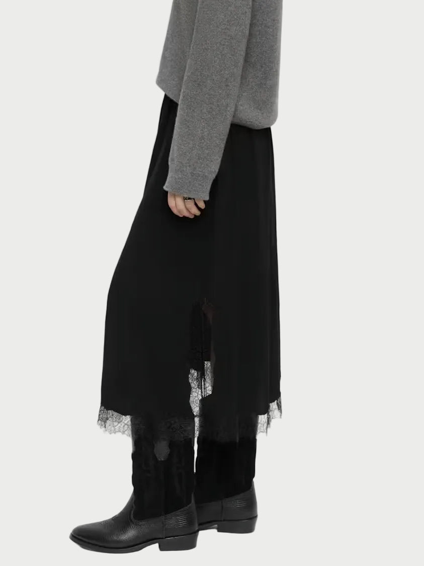 A woman modeling a gray knit sweater and a long black skirt with tulle trim, paired with black boots, against a plain light gray studio background.