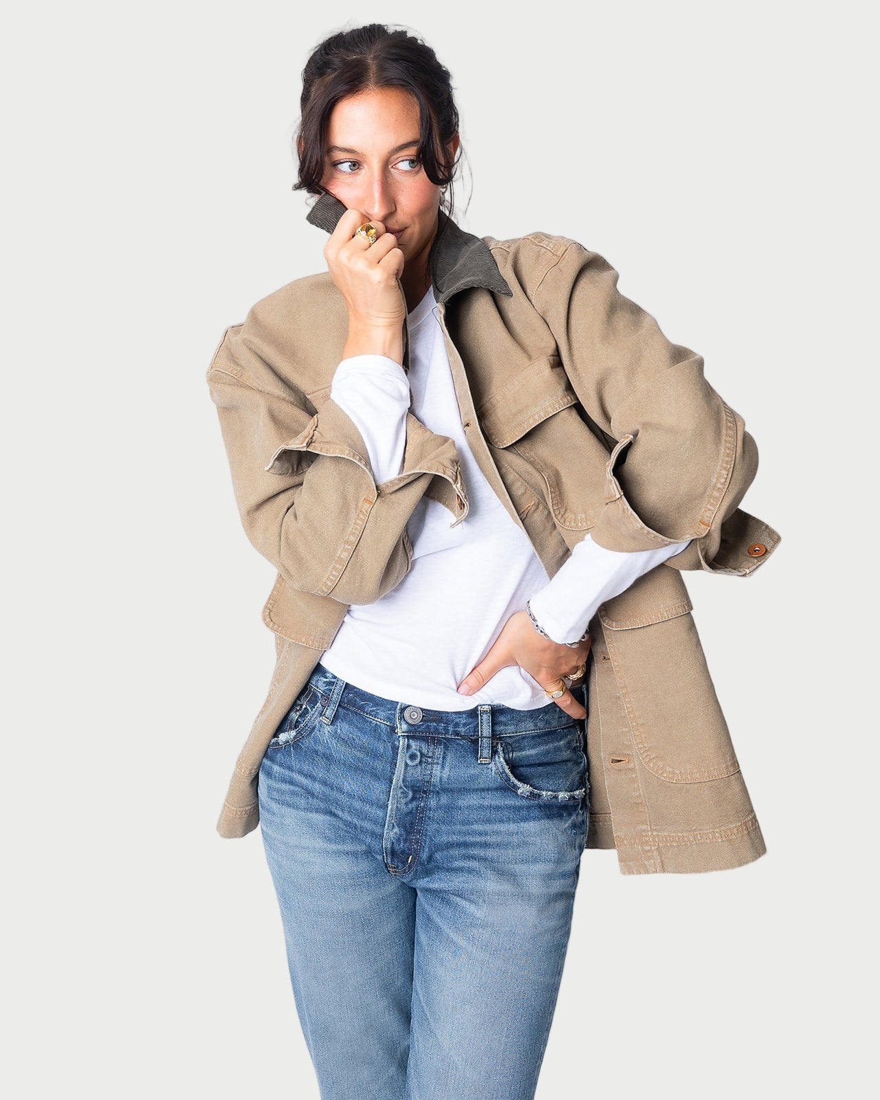 A woman poses against a light background, holding the corduroy collar of her beige SLVRLAKE Hayden Chore Jacket to her face with one hand, while her other hand rests in her pocket over a white shirt and blue jeans.