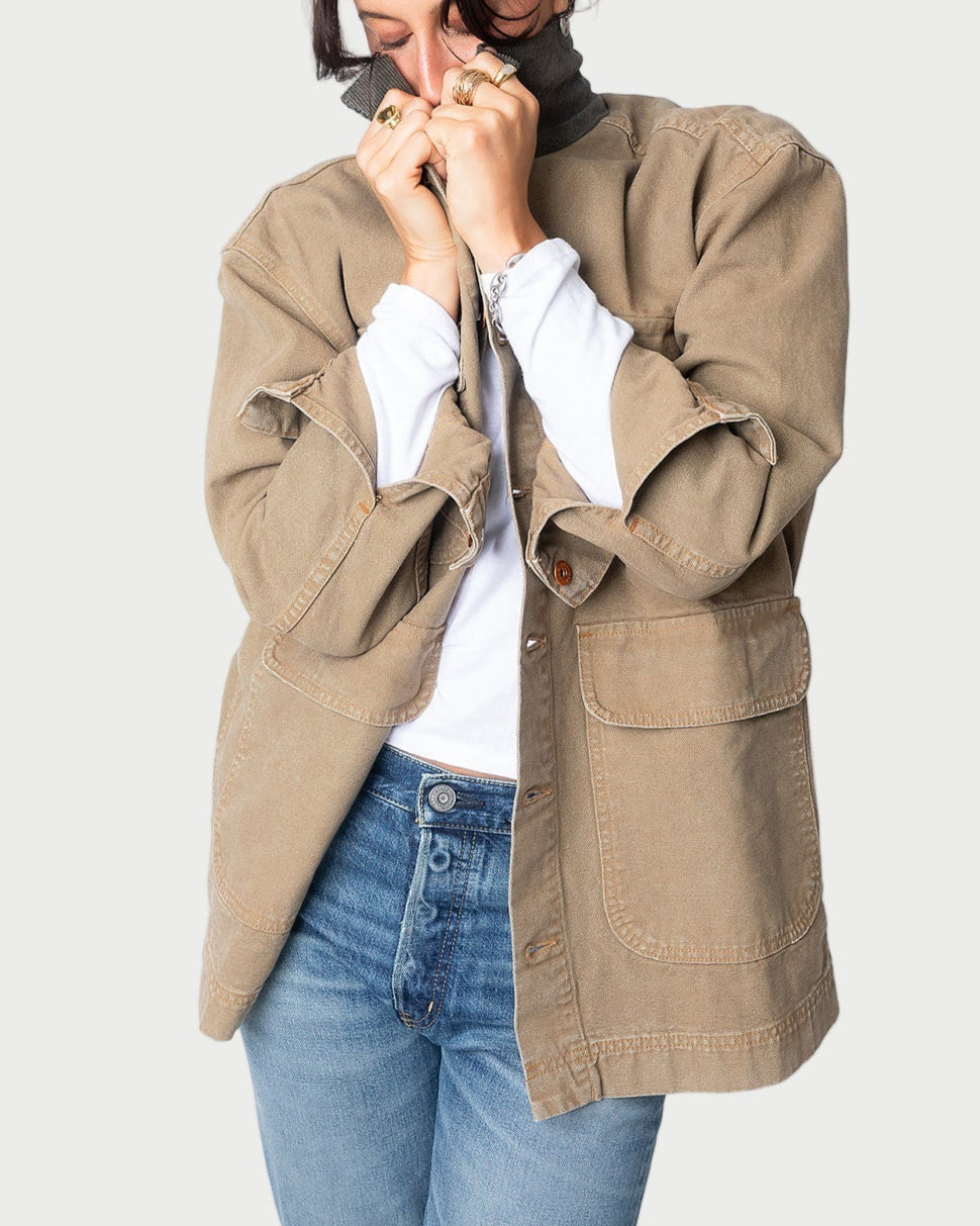A person wears the SLVRLAKE Hayden Chore Jacket by SLVRLAKE, featuring a loose fit and corduroy collar, layered over a white shirt and blue jeans. They stand with hands near their face against a plain white background.