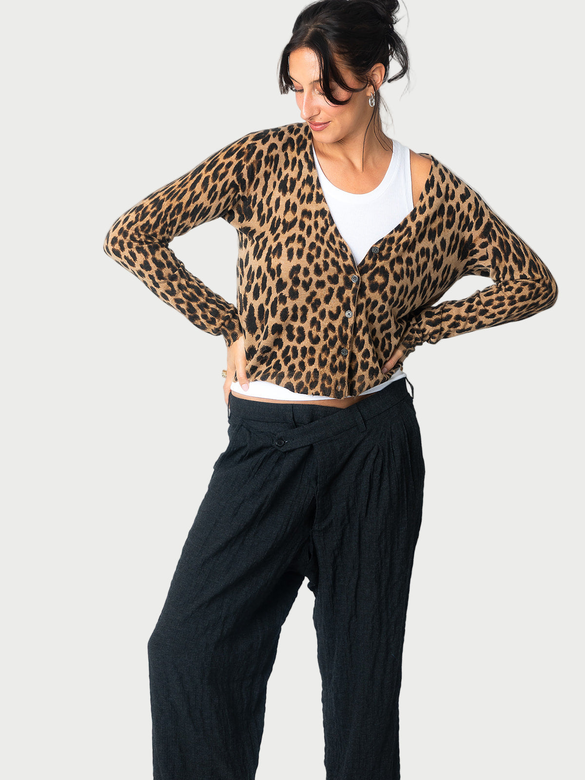 A woman stands with her hands on her hips, wearing the Zadig & Voltaire Leopard Print Cardigan over a white top and loose black pants, set against a plain light background.