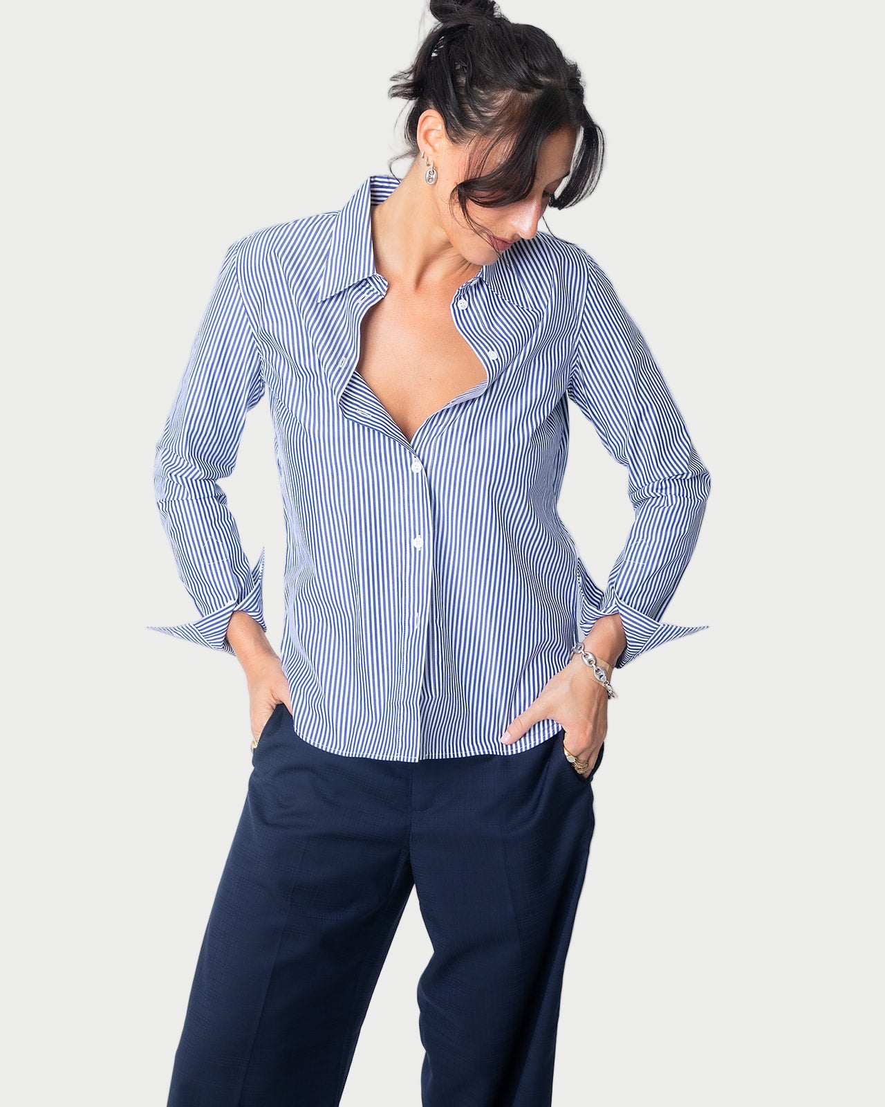 A woman models the WE-AR4 Fitted Collared Shirt in limited edition blue and white, paired with navy pants. She stands with hands in her pockets, looking down with a slight smile against a plain white background.
