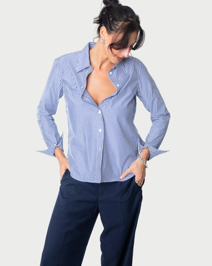 A woman models the WE-AR4 Fitted Collared Shirt in limited edition blue and white, paired with navy pants. She stands with hands in her pockets, looking down with a slight smile against a plain white background.