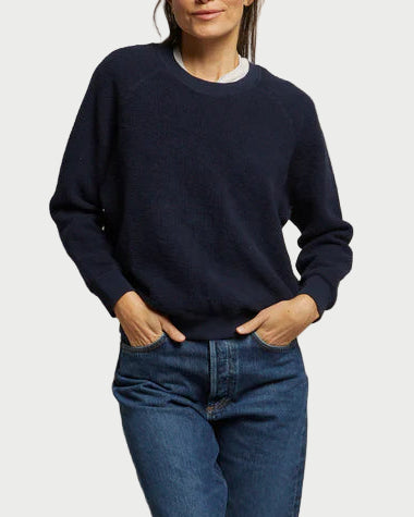 Woman wearing a navy sweater and blue jeans against a plain background