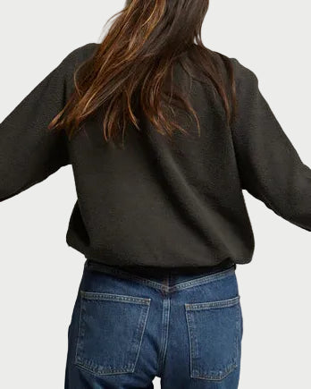 Person wearing a black sweater and blue jeans against a plain background