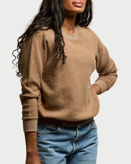Woman wearing a brown sweater and blue jeans against a plain background
