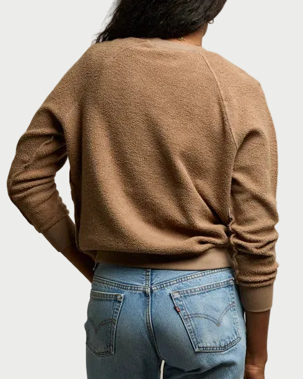 Person wearing a brown sweater and blue jeans against a plain background