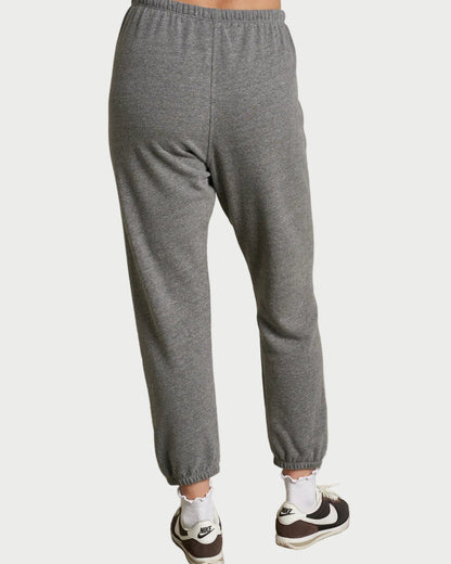 Person wearing gray sweatpants and black and white sneakers on a plain background