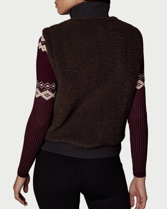Woman wearing a brown vest with patterned sleeves against a textured gray background