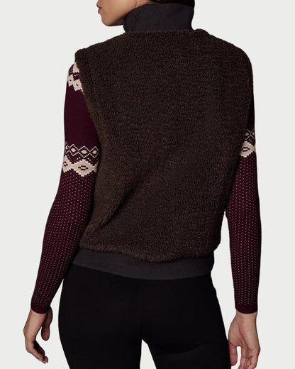 Woman wearing a brown vest with patterned sleeves against a textured gray background
