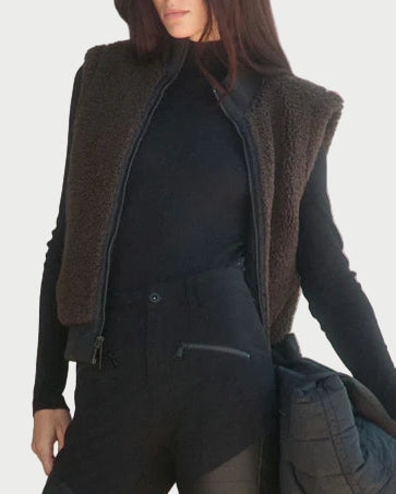 Person wearing a black outfit with a brown jacket standing on steps.