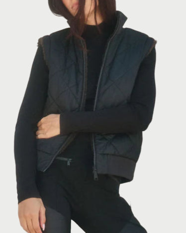 Person wearing a black outfit with a vest, standing against a neutral background.