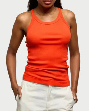 Woman wearing an orange tank top and white pants against a plain background