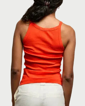 Person wearing an orange tank top and white pants against a plain background