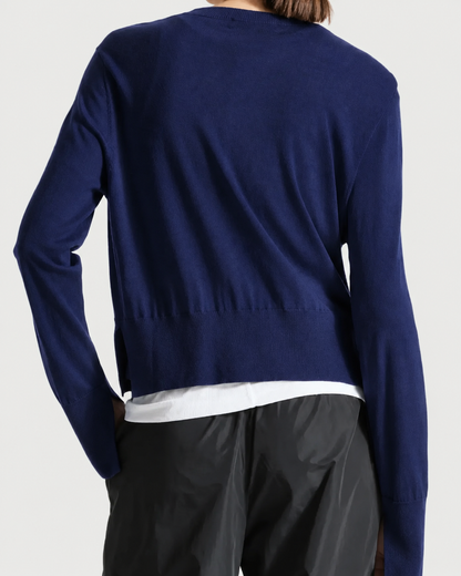 A person shown from the back wearing a navy blue long-sleeve knit sweater over a white shirt and dark pants, against a light gray studio background.