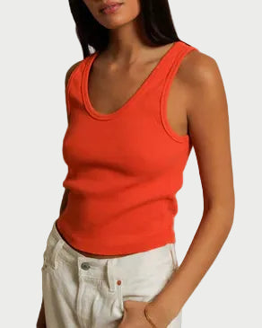 Woman wearing an orange tank top and white pants against a plain background