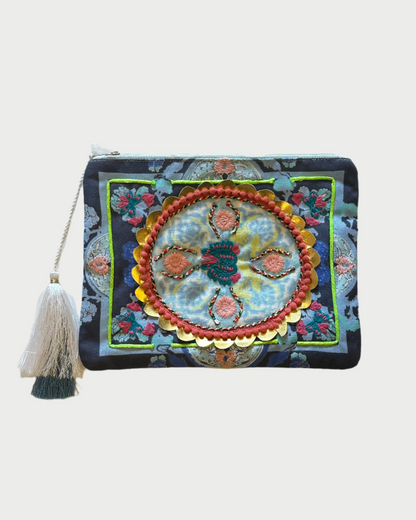 The DEBBIE KATZ Boho Pouch is a decorative accessory with intricate floral and circular patterns, featuring embroidered details, a tassel in one corner, and a vibrant mix of blue, orange, yellow, and green—ideal for your beach essentials.