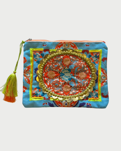The DEBBIE KATZ Boho Pouch is a vibrant accessory with intricate embroidery on a blue fabric. It features an ornate central design in orange, gold, and green, plus a multicolored tassel on the zipper, perfect for beach bag essentials.