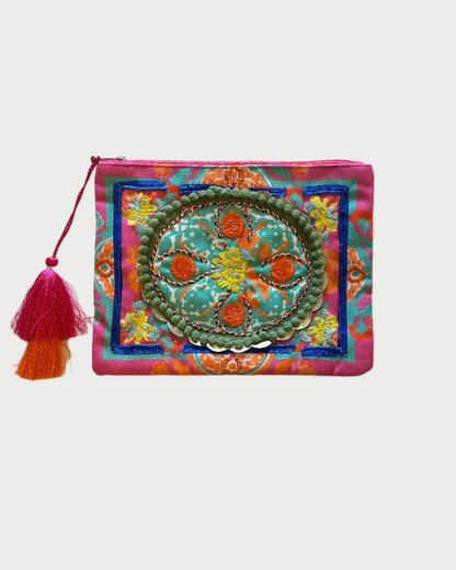 The Debbie Katz Boho Pouch features a vibrant design with colorful embroidery, a pink zipper, and a red and orange tassel. Green, orange, and yellow create circular and floral motifs on the pouch's vibrant backdrop—ideal for storing beach bag essentials.
