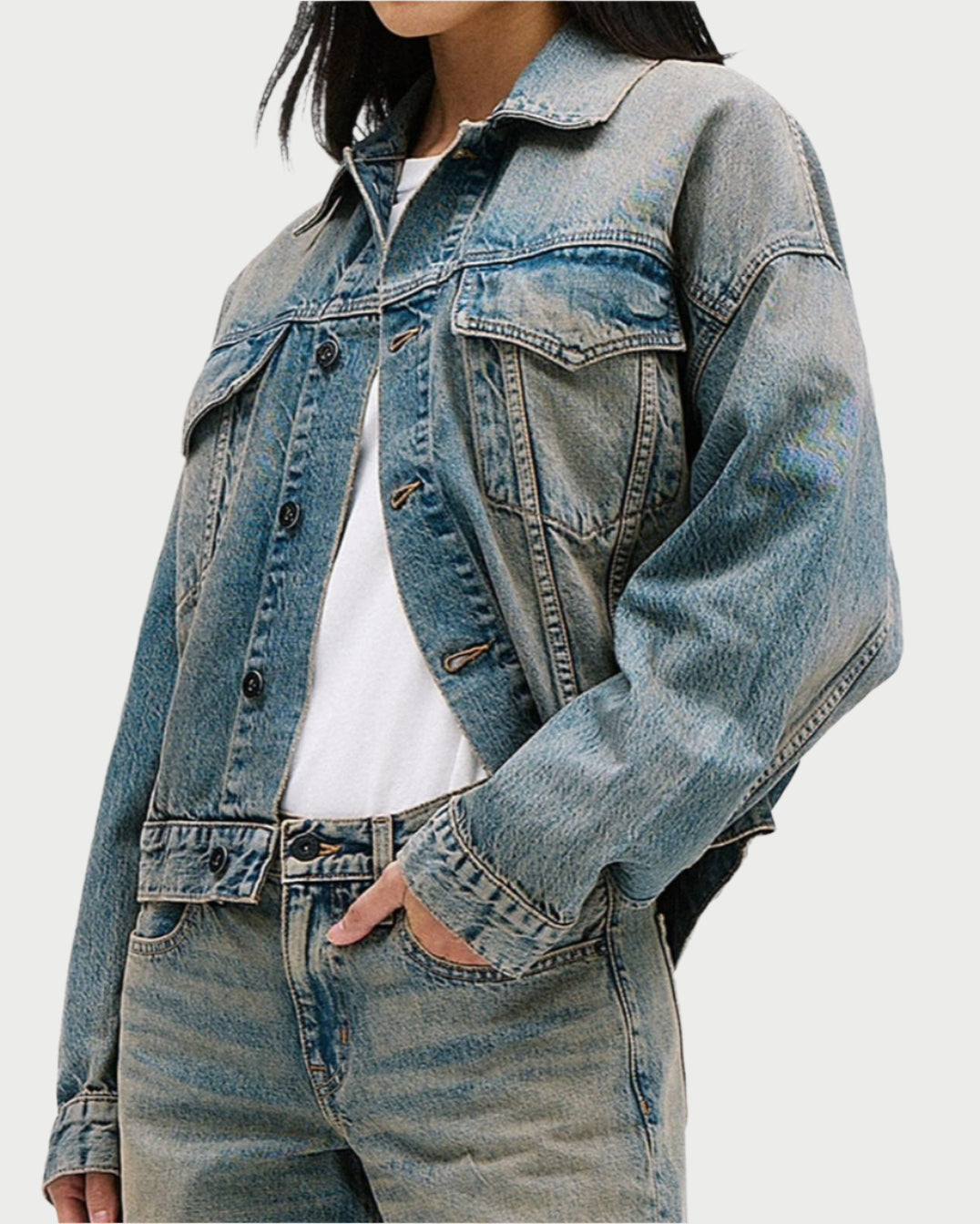 A person in an oversized silhouette dons the SLVRLAKE Boston Trucker Jacket and classic blue denim jeans. Their white shirt subtly shows, hands resting casually in jacket pockets. The image is cropped just above the shoulders for a striking effect.
