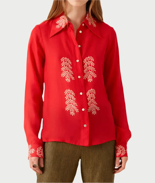 A person wears the cherry-colored Patti Embroidered Shirt from Alix of Bohemia, adorned with white embroidered leaf patterns on the front and cuffs. Made from TENCEL™ Lyocell, it features a pointed collar and long sleeves for a distinctive style, complemented by olive green pants.