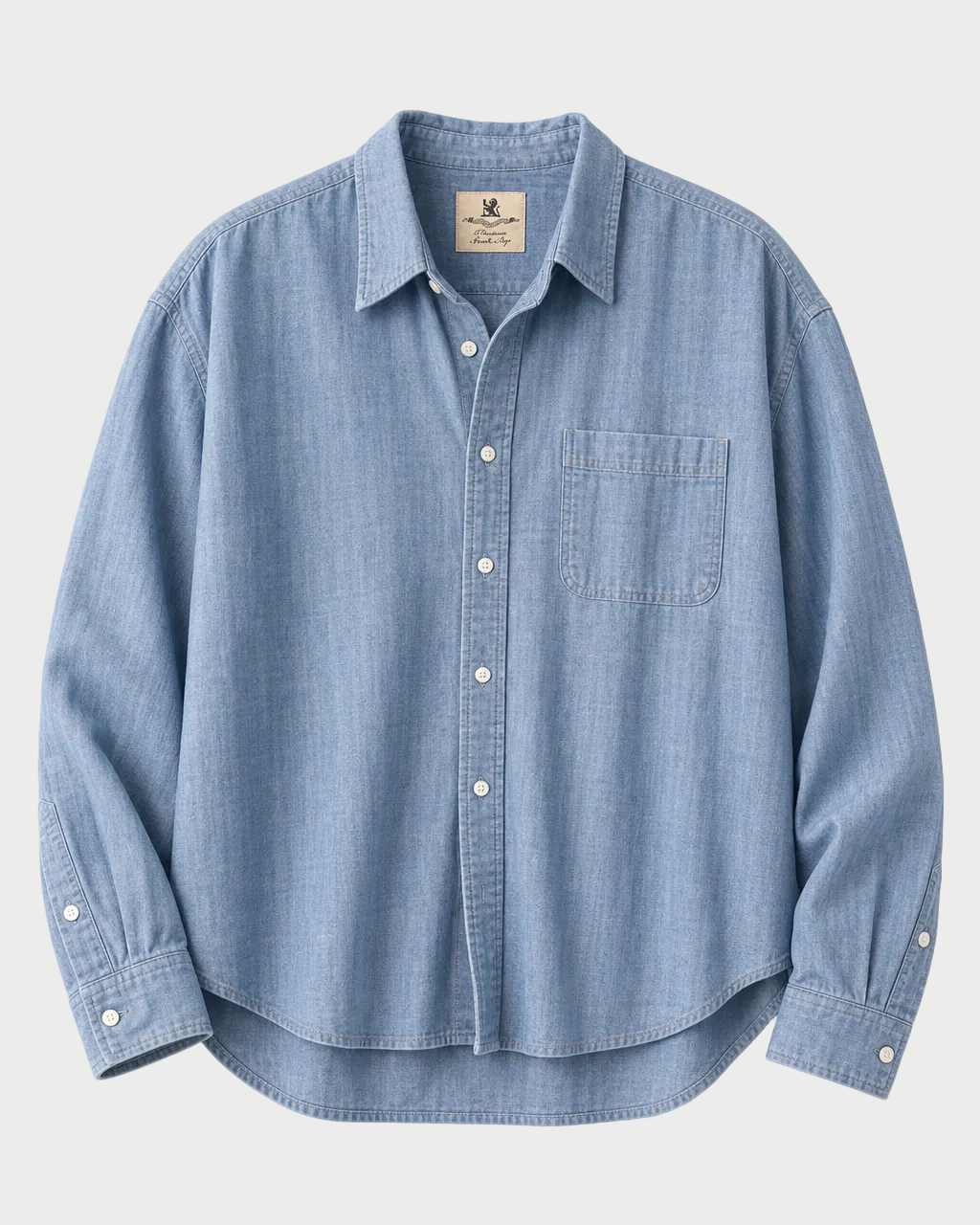 A light blue chambray button-down shirt with a chest pocket, laid flat against a light beige background.