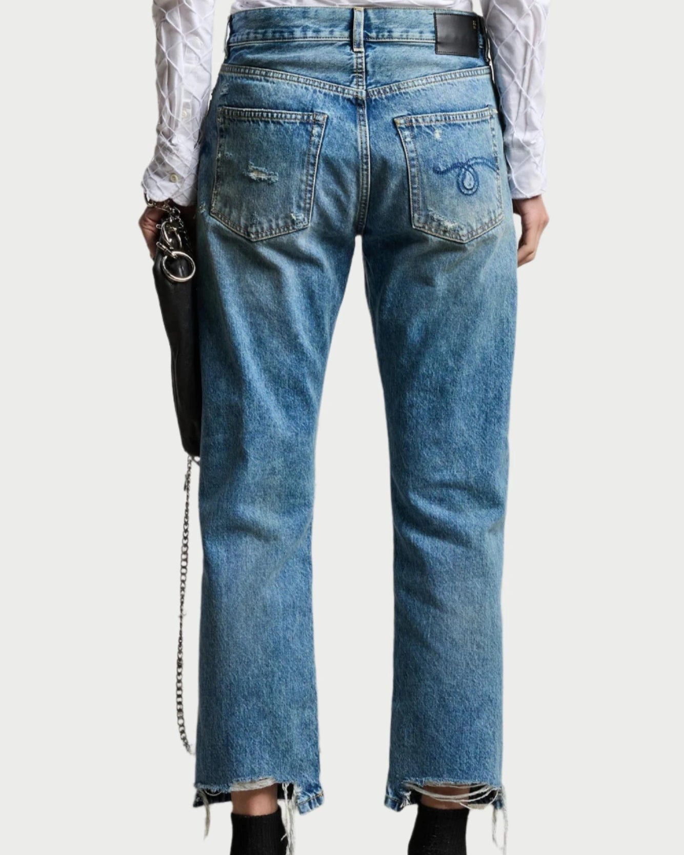 Person wearing blue jeans with a white shirt on a plain background