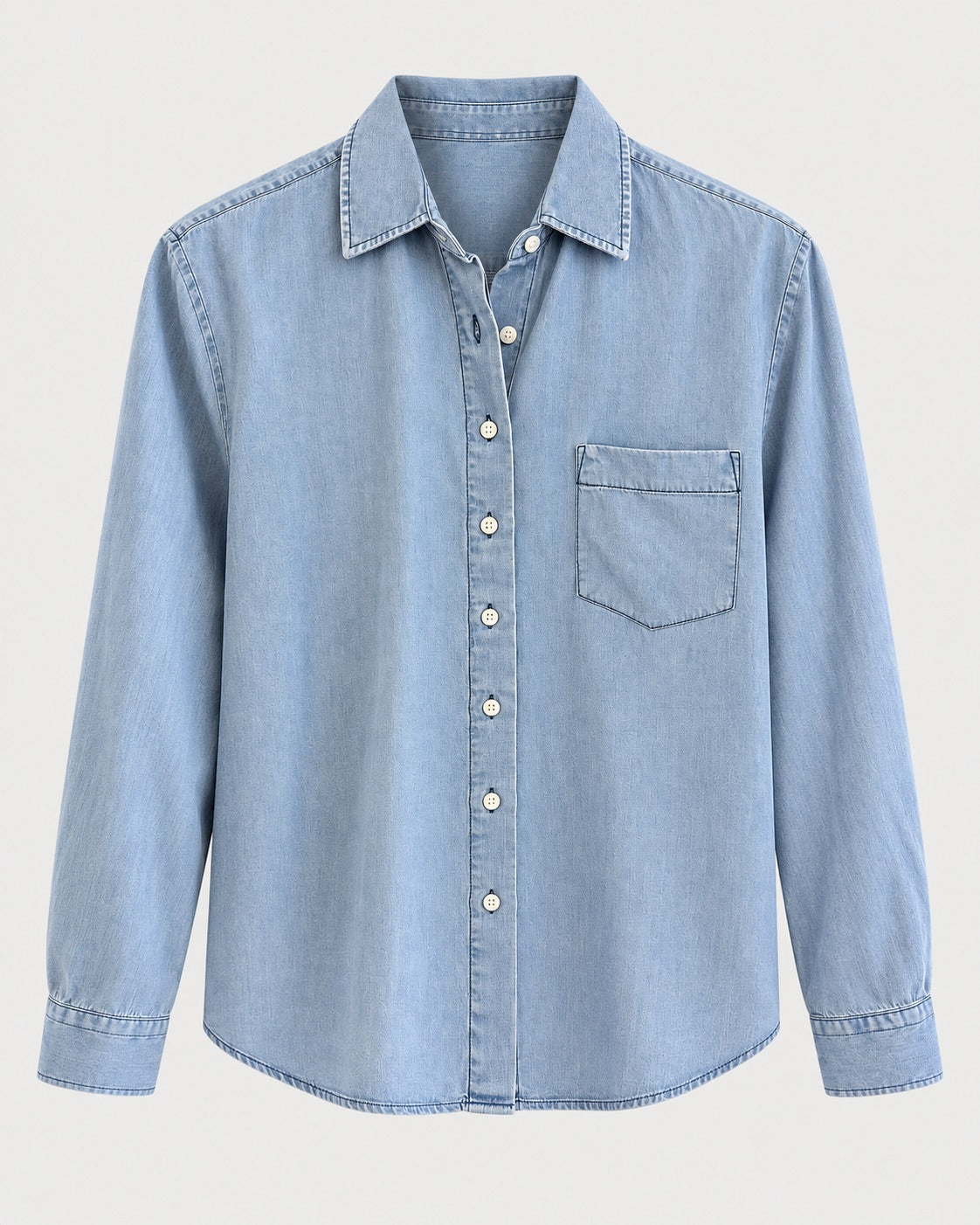 The Shirt Long Sleeve Boxy Crop by The Shirt is a light blue denim women’s cotton shirt featuring a button-down front with a no gape button, a single chest pocket on the left, and a classic collar, displayed against a plain background.