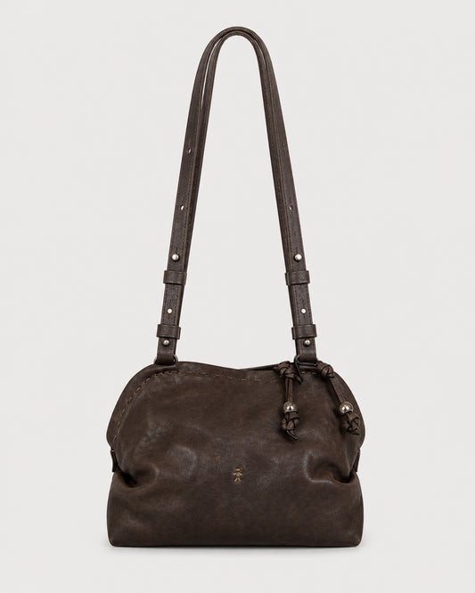The Henry Beguelin Leather Bolla Bassa Bag is a dark brown Italian leather shoulder bag featuring adjustable double straps with decorative knots and a subtle embossed Henry Beguelin logo on the front. Handcrafted with a simple, slightly gathered design, it is showcased against a plain white background.