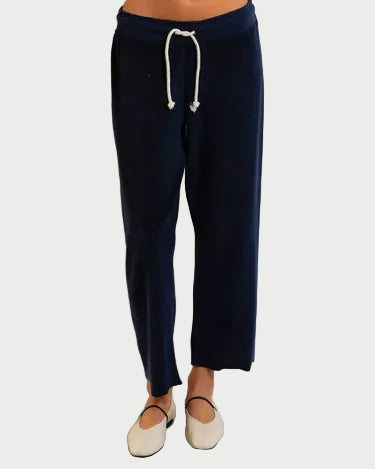 A person wears perfectwhitetee’s Eliana Drawstring Pant in navy blue loop terry cotton, styled with cream flats, shown waist down against a plain light background.