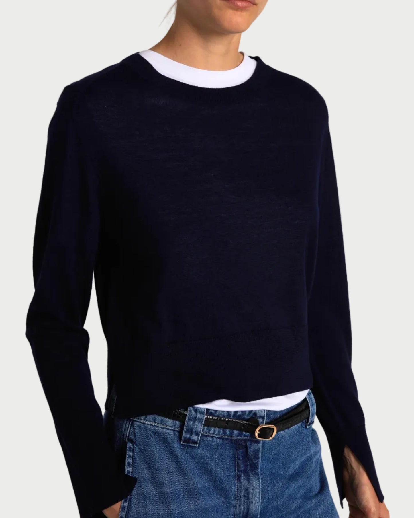 A person wears a Saint Art NY Elodie Sweater Navy over a white crew-neck shirt, paired with blue jeans and a black belt. Their head is partially out of frame.