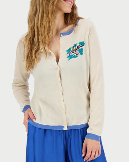 Woman wearing a cream cardigan with a blue design and a long blue skirt on a white background