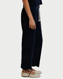 Woman wearing a navy blue sleeveless top and wide-leg pants against a white curtain backdrop