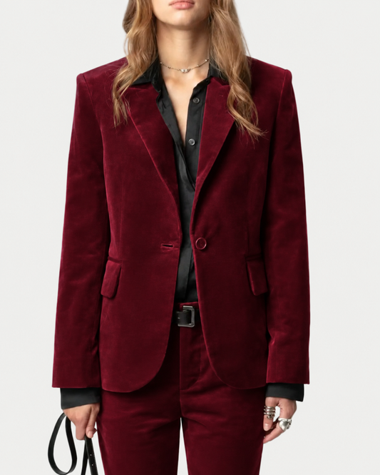 A person is pictured from the knees up against a plain background, wearing the Zadig & Voltaire Vavy Velvet Blazer in rich red with a single-button closure over a black shirt and holding a black strap.