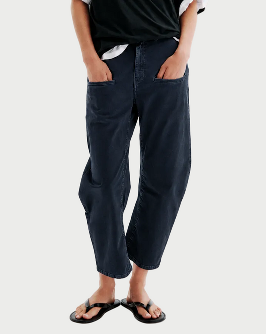 Person wearing navy All lll Kenny Pant navy blue barrel-leg jeans with front pockets and black flip-flops.