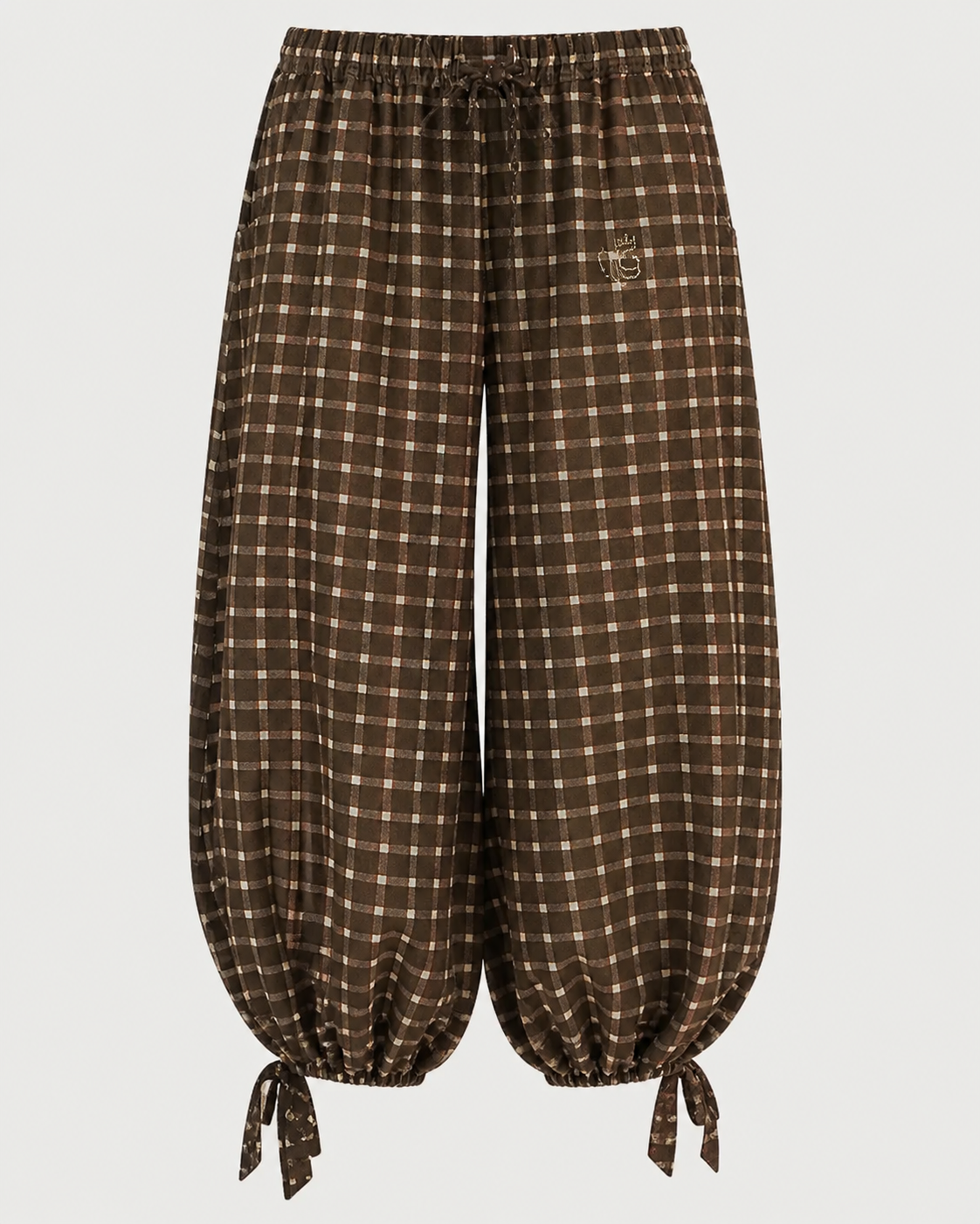 The ME369 Isla Balloon Pant by ME369 features a brown plaid design with a drawstring elastic waist and cuffs that tie at the ankles. Crafted from viscose, these pants showcase a light-colored checked placement print and include a small embroidered logo on the left hip.