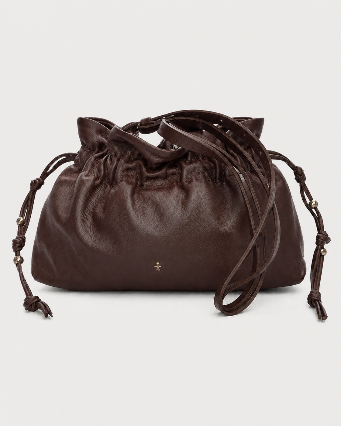 The Henry Beguelin Floriana Clutch by Henry Beguelin is a dark brown luxury handbag crafted from supple Italian leather, featuring a gathered top, long adjustable straps, and elegant gold bead accents. A small gold emblem decorates the bottom center of this handcrafted bag, displayed against a plain light background.