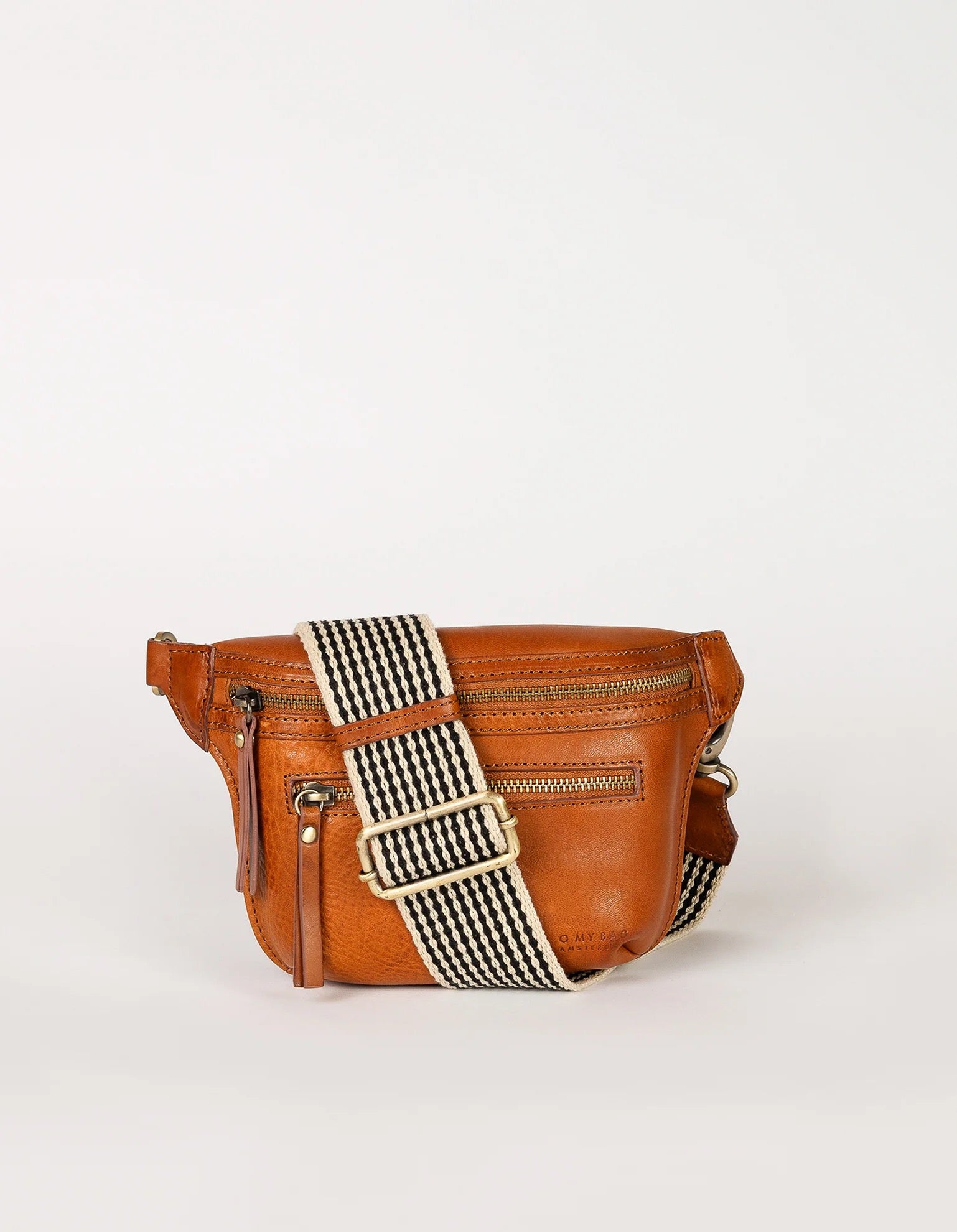 The Beck's Bum Bag in Cognac by O MY BAG features a front zipper pocket and a wide, black-and-white striped adjustable strap, shown against a plain white background.