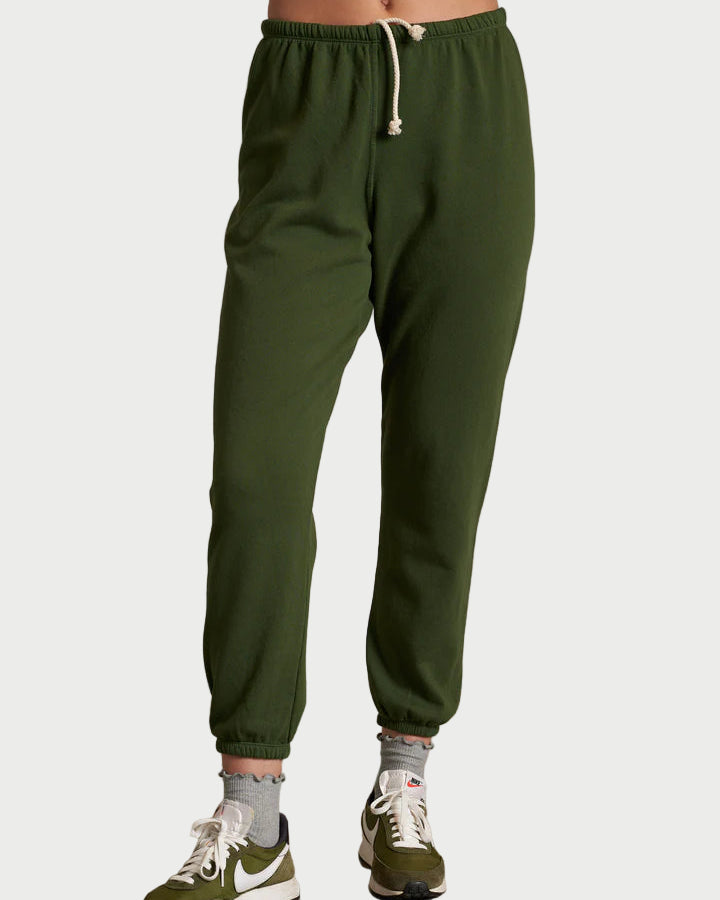 Person wearing green sweatpants and matching sneakers on a plain background