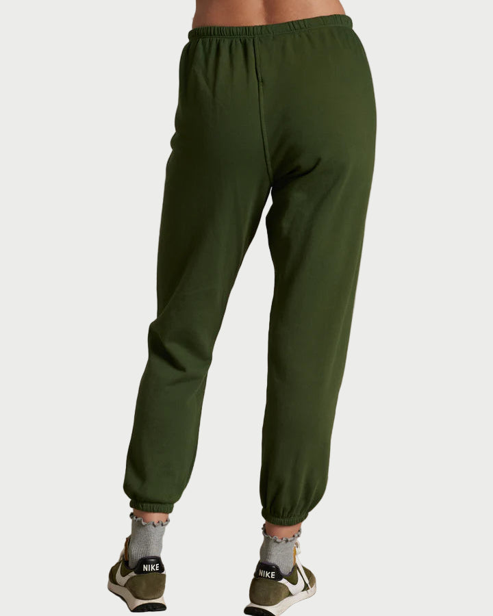 Person wearing green sweatpants and gray sneakers on a plain background