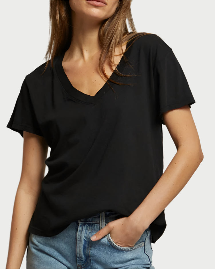 Clad in perfectwhitetee's Hendrix Basic V-Neck T-Shirt in Black and light blue jeans, an individual stands casually with one hand in a pocket against a neutral background, face not visible.