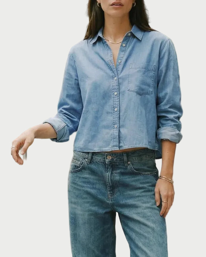 A woman wearing a light blue The Shirt Long Sleeve Boxy Crop with long sleeves, rolled cuffs, and blue jeans.