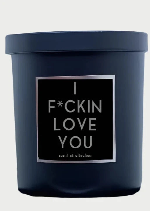 A black Rude Dude Candles candle labeled "I F*CKIN LOVE YOU" in white text sits beside a metallic hand sculpture displaying its middle finger. This bold statement piece, a 9oz beauty, is proudly made in the USA by Rude Dude.
