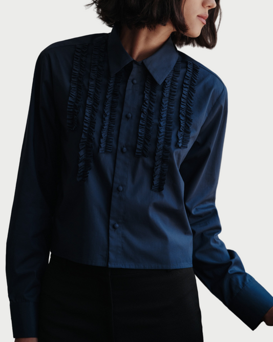 Woman wearing a blue blouse with ruffled details against a neutral background