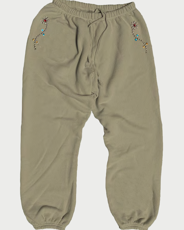 The Madeworn Flower Power Sweatpant from Madeworn features a beige hue, elastic waist, gathered ankles, and colorful embroidered floral designs near the front pockets—vintage unisex style with true flower power energy.