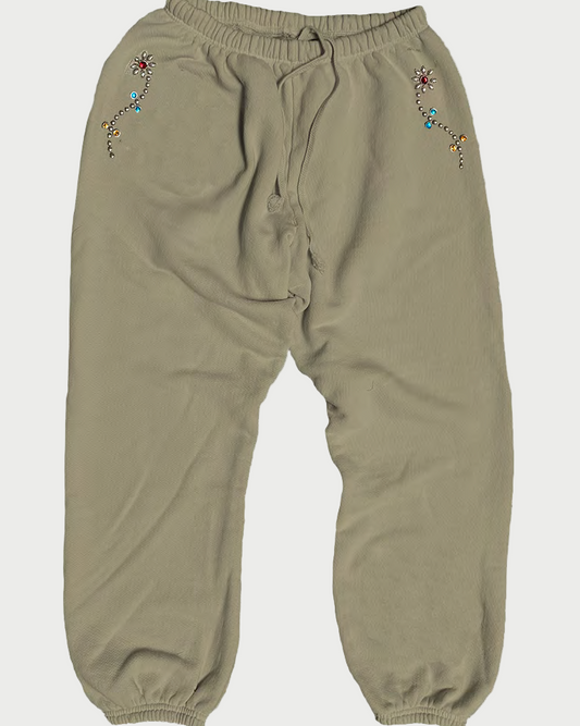 The Madeworn Flower Power Sweatpant from Madeworn features a beige hue, elastic waist, gathered ankles, and colorful embroidered floral designs near the front pockets—vintage unisex style with true flower power energy.