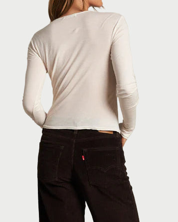 Person wearing a white long-sleeve shirt and dark pants against a plain wall.