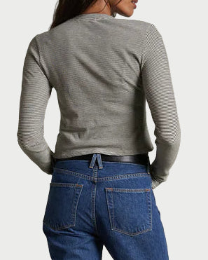 Person wearing a gray sweater and blue jeans standing against a plain white wall.