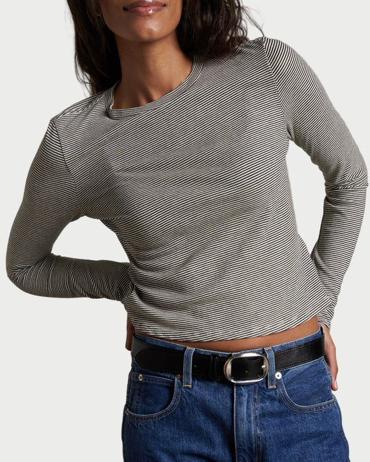 Woman wearing a gray long-sleeve top and blue jeans against a plain background