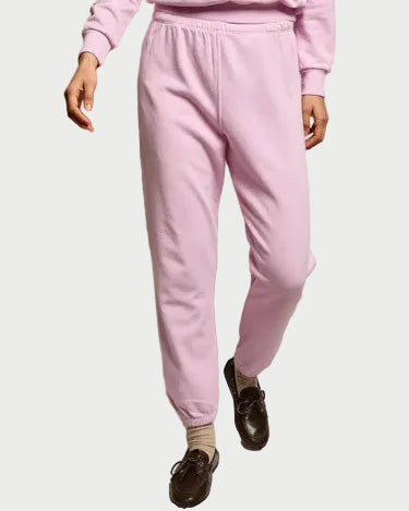 Person wearing a pink tracksuit with brown shoes on a plain background